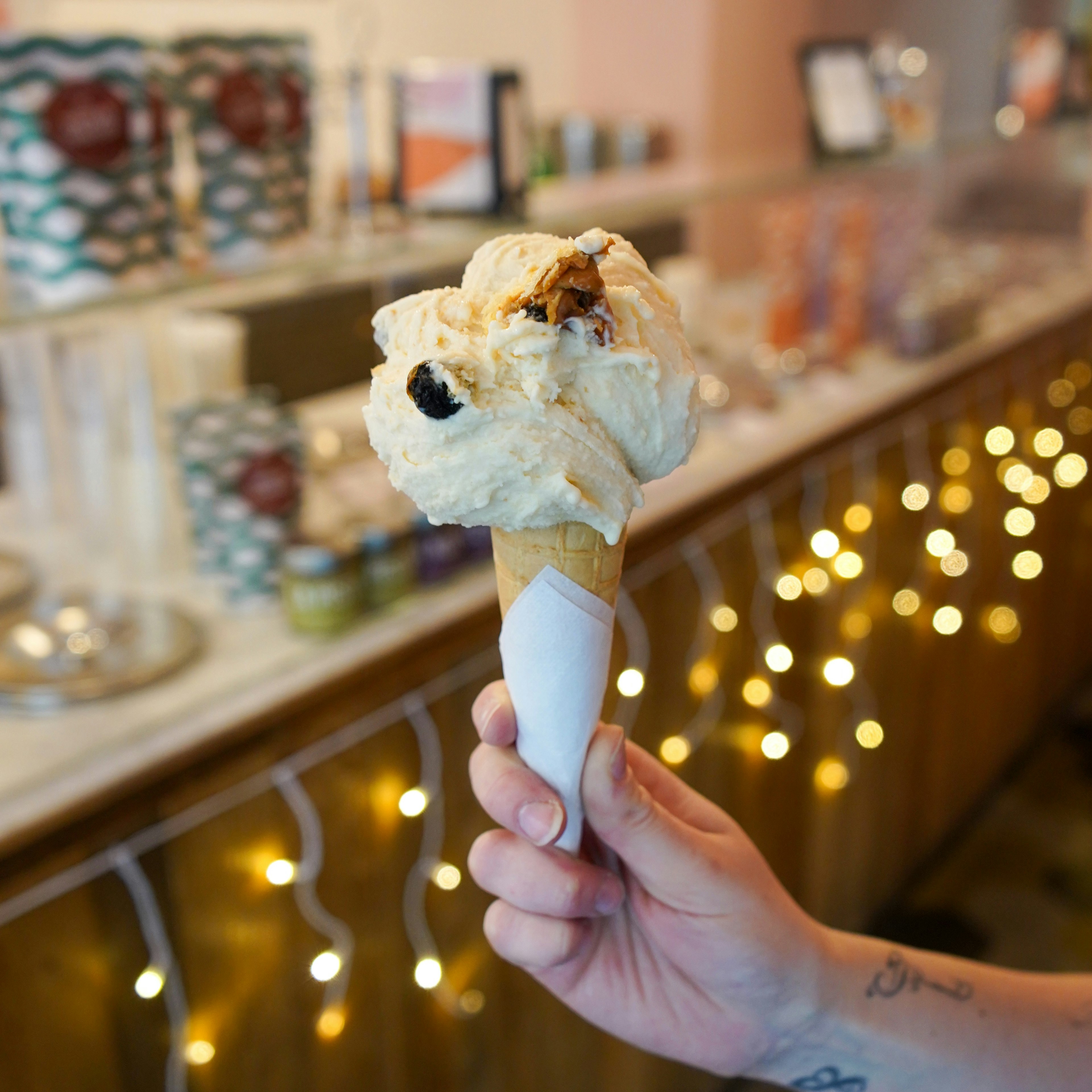 A person holds a cone with gelato in front of festive strung lights at Pavé Milano Gelateria